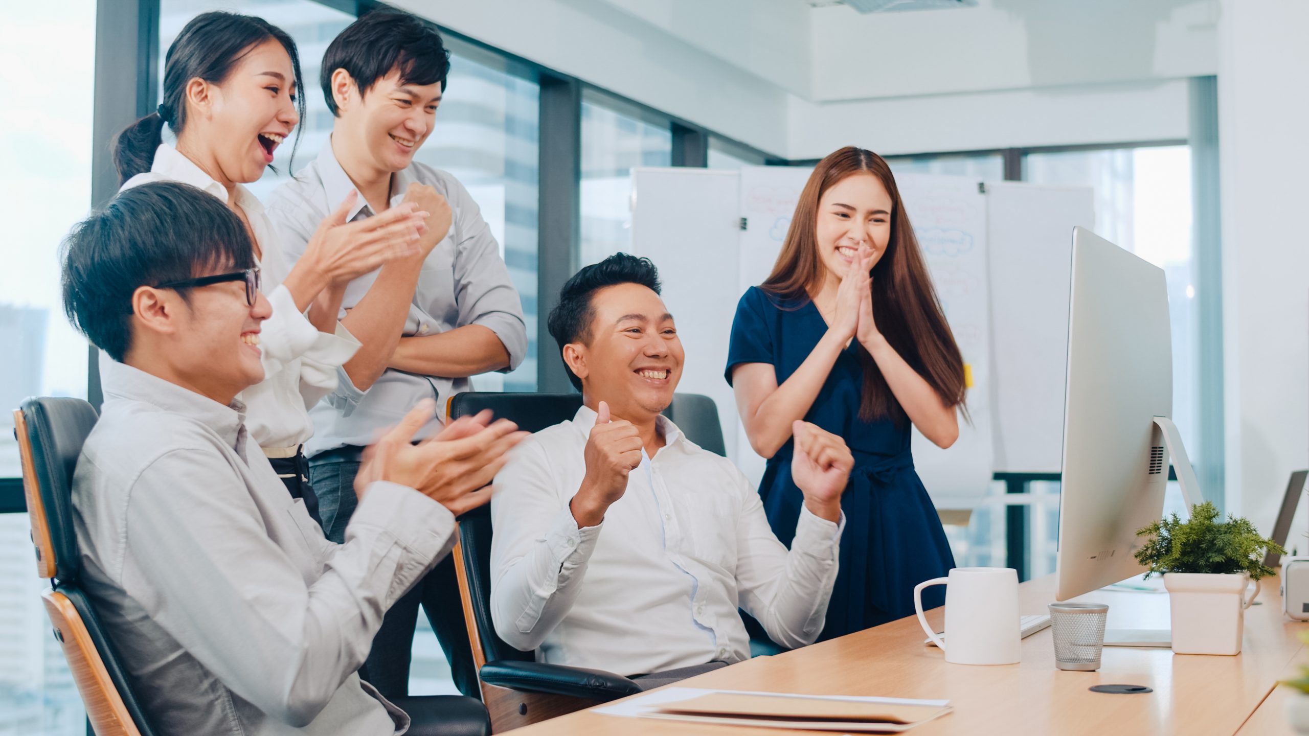 Millennial group of young businesspeople Asia businessman and businesswoman celebrate giving five after dealing feeling happy and signing contract or agreement at meeting room in small modern office.