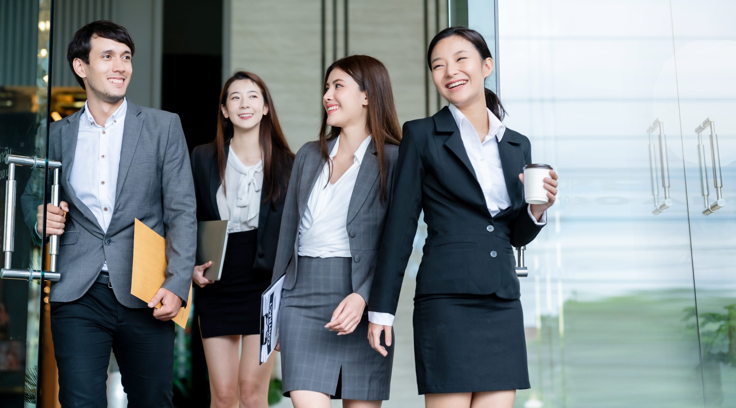group of smart young asian businessmale and female formal dress walking pass modern office entrance with confident and happiness